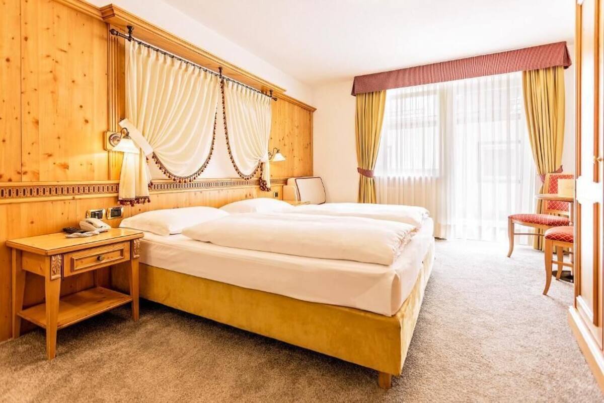 A hotel room with a large bed, wooden paneling, a desk with a telephone, and a chair.