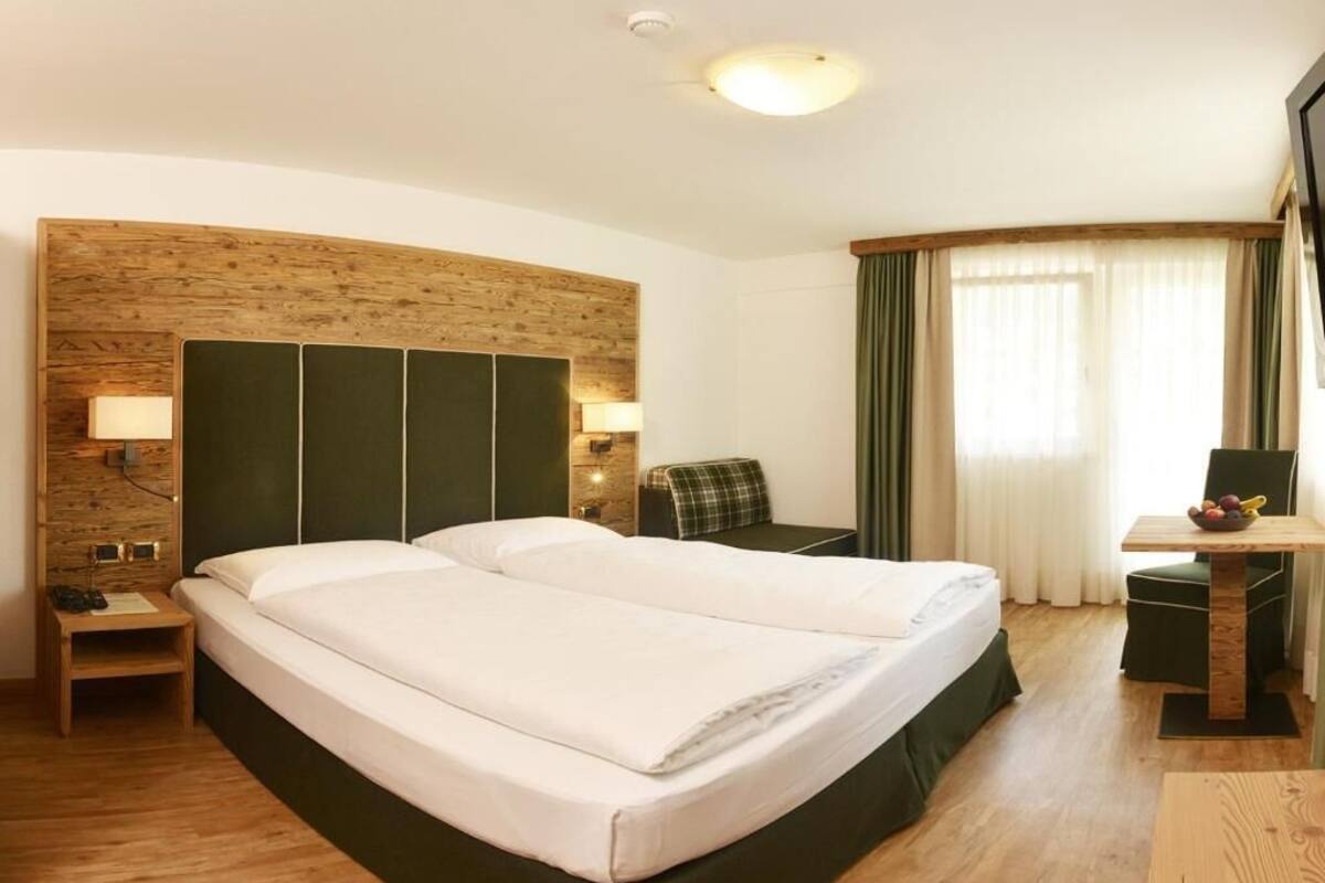 A hotel room with a large bed, a desk, a chair, a lamp, and a window with curtains.
