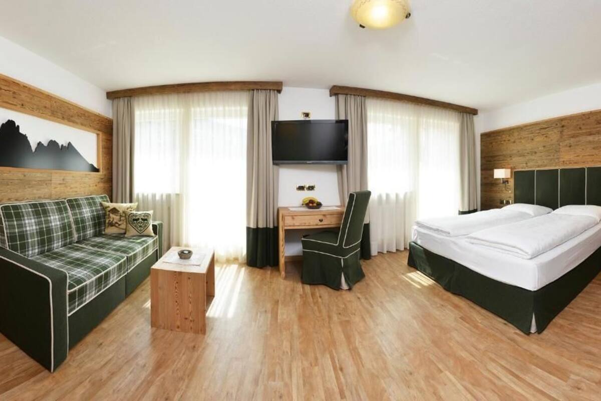 A hotel room with a bed, a desk, a chair, a sofa, a TV, and curtains.