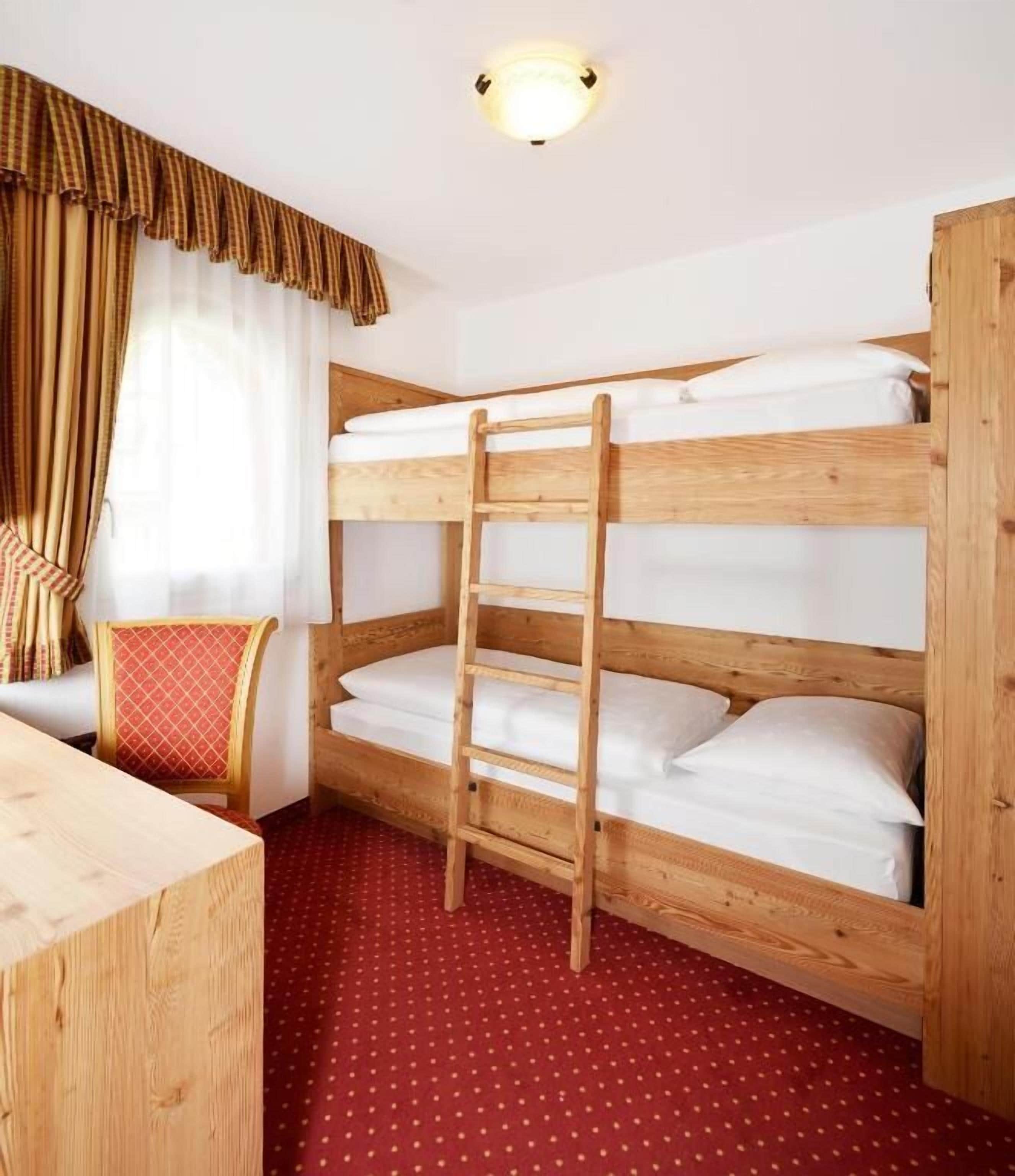 A bunk bed with a ladder, a wooden desk, a chair with a red cushion, and a red polka dot carpet.