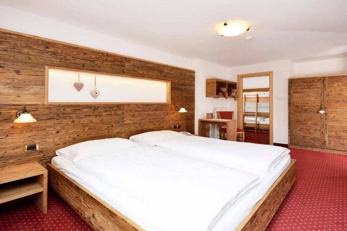 A double bed with a wooden headboard, a bedside table, a desk with a chair, a wardrobe, and a mirror.