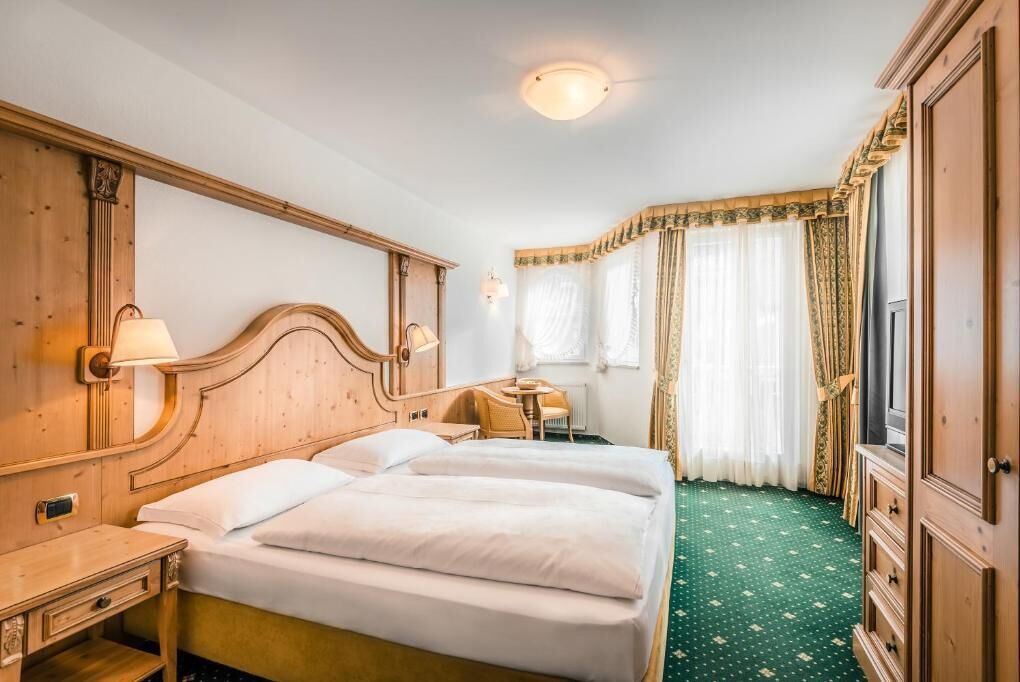 Ein Hotelzimmer mit zwei Betten, einem Schreibtisch, einem Stuhl, einem Kleiderschrank und einem fenster mit Vorhängen.