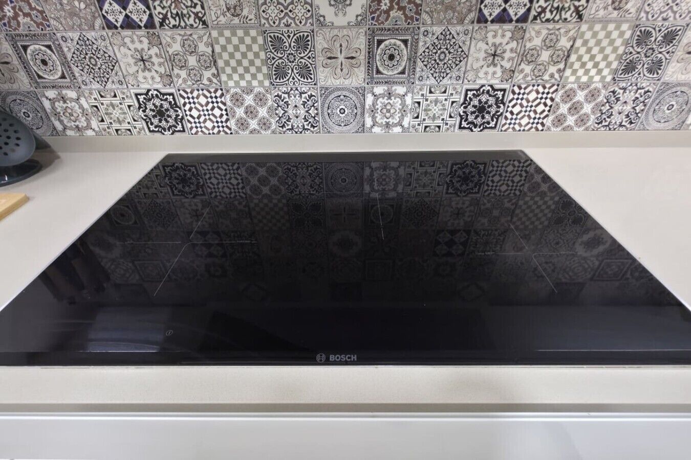 Un piano cottura a induzione Bosch con una schiena a parete bianca caratterizzata da una varietà di decori di piastrelle elaborate.
