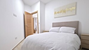 Ein Schlafzimmer mit einem Bett, einem Nachttisch, einer Holztür und einem an der Wand befestigten Kunstwerk.