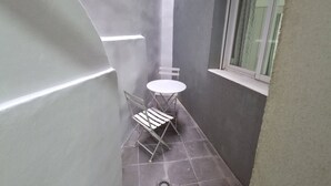 Ein schmaler Balkon mit einem kleinen Tisch und zwei Stühlen, einem Fenster und einer Tür.