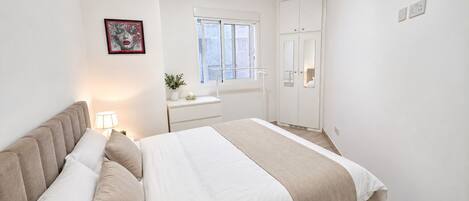 A bedroom with a bed, bedside table, lamp, window, and wardrobe.