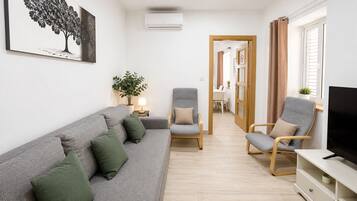 Una sala de estar con un sofá gris, dos sillones, un mueble para televisión y una planta en maceta.