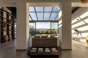 Ein modernes Interieur mit einem großen Fenster, einem Korbssessel und einem Bücherregal mit Dekoration.