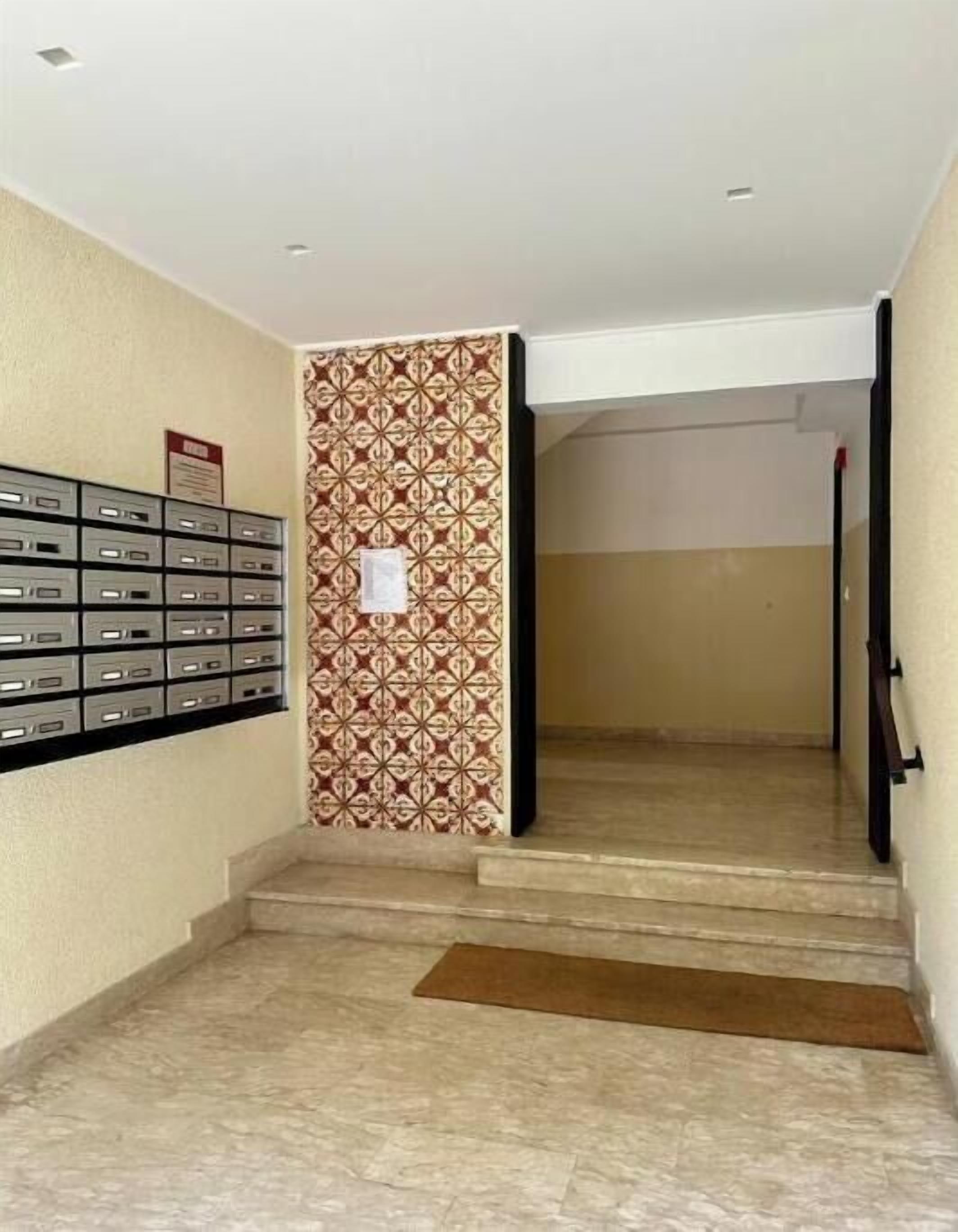 A hallway with a patterned wall, a row of mailboxes, and a staircase leading to another area.