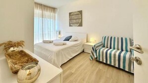 A bedroom with a bed, bedside table, lamp, and a striped sofa.