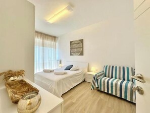 Een slaapkamer met een bed, nachtkastje, lamp en een gestreept slaapbankje.