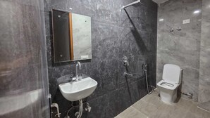 A bathroom with a sink, mirror, shower, and toilet. - Hotel Mannat Inn (New Delhi)