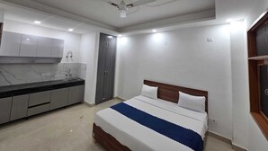 A bedroom with a bed, a ceiling fan, a built-in wardrobe, and a kitchen area with cabinets and a countertop. - Hotel Mannat Inn (New Delhi)