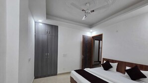 A bedroom with a bed, a wardrobe, a ceiling fan, and a door leading to another room. - Hotel Mannat Inn (New Delhi)