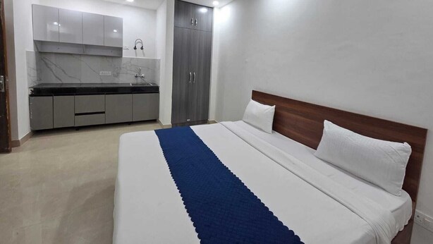 A bedroom with a bed, a blue and white striped blanket, a wooden headboard, and a white pillow. - Hotel Mannat Inn (New Delhi)