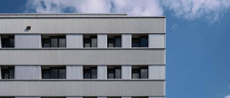 Un edificio de varios pisos con un diseño arquitectónico moderno, que presenta una serie de balcones y ventanas.
