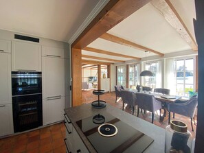 Eine moderne Küche mit integrierten Geräten, ein Essbereich mit Tisch und Stühlen und große Fenster, die viel Tageslicht hereinlassen.
