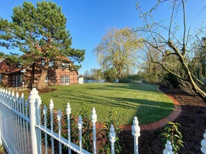 Ein Haus mit gepflegtem Rasen, einem weißen Zaun und einem großen Baum im Hintergrund.