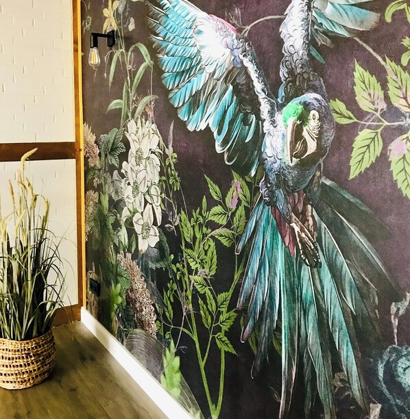 A mural of a parrot with vibrant feathers, surrounded by lush foliage and flowers. - Country house by the lake between Hamburg and Lüneburg (Winsen (Luhe))