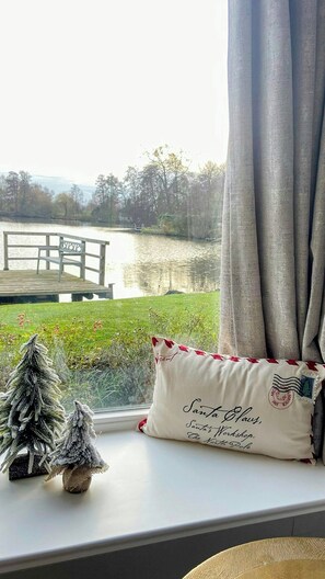 Ein Fenster mit Blick auf einen See, eine Holzsteg und ein Kissen mit Weihnachtsmann-Motiv.