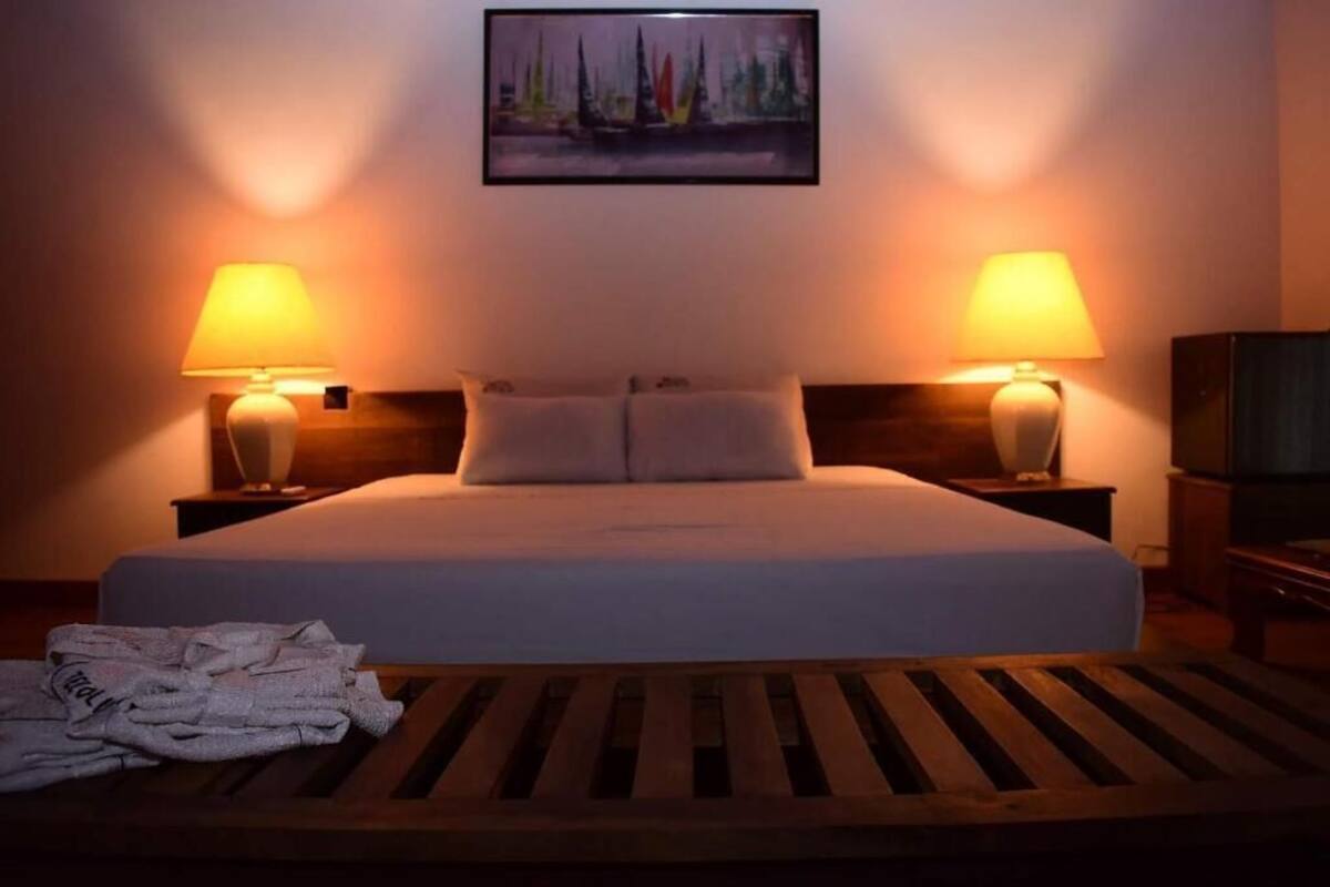 Habitación de hotel con una cama grande, dos lámparas de noche, un cuadro en la pared y un banco de madera con toallas.