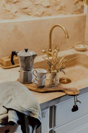 Eine Küchenarbeitsplatte mit einer Kaffeemaschine, einer Tasse und einer Vase mit Trockenpflanzen.