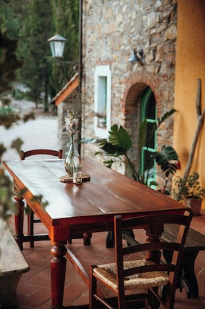 Ein Holztisch mit Stühlen, eine Vase mit Blumen und ein Steinhaus im Hintergrund.
