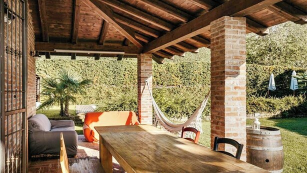 An outdoor patio with a wooden table, a hammock, and a brick pillar.