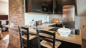 A modern kitchen with dark cabinets, a stainless steel refrigerator, a brick accent wall, and a wooden island with bar stools.