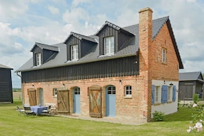 A two-story brick house with a sloped roof, a front porch with a table and chairs, and a small garden area. - Farmhouse comfort in the Uckermark region (Weggun)