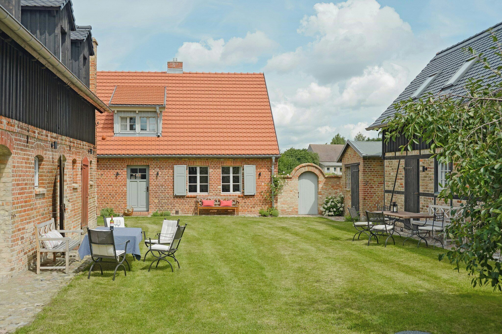 A brick house with a red-tiled roof, a small front yard with a lawn, and a patio with outdoor furniture.