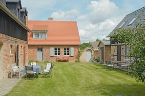 A brick house with a red-tiled roof, a small front yard with a lawn, and a patio with outdoor furniture. - Farmhouse comfort in the Uckermark region (Weggun)