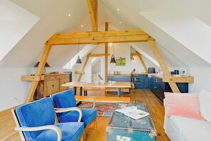 A loft-style room with a dining table, blue chairs, a white sofa, and a kitchen area. - Farmhouse comfort in the Uckermark region (Weggun)