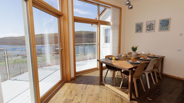 A dining area with a table set for four, large windows, and a view of the outdoors. - NEW to VRBO: Spacious House w/ Coastal Views & Private Garden (Whiteness)