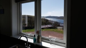 A window with a view of a body of water, a building, and a grassy area. - NEW to VRBO: Spacious House w/ Coastal Views & Private Garden (Whiteness)