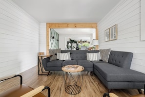 Una sala de estar moderna con un sofá seccional gris, una mesa de centro redonda de madera y un taburete de metal negro.