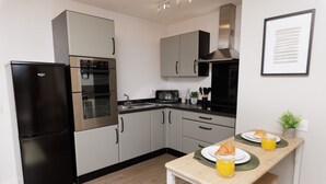 Eine moderne Küche mit einem schwarzen Kühlschrank, einem Edelstahl-Backofen und einer Mikrowelle. Ein Esstisch ist mit zwei Tellern und einem Glas Orangensaft gedeckt.