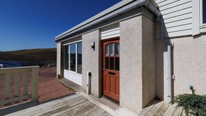 Ein Haus mit einer Holterrasse, einer roten Tür und einem Fenster.