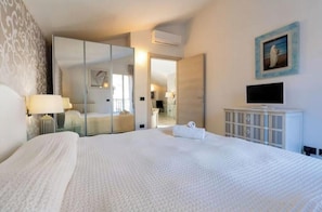 Ein Hotelzimmer mit einem großen Bett, einem Fernseher, einem Spiegel und einem Bild an der Wand.