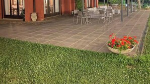 Un edificio con un patio, mobiliario exterior y un jardín con flores rojas.