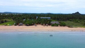 A beach resort with a sandy shoreline, a few huts, and a distant hill. - NN Beach Resort Nilaveli (Trincomalee)