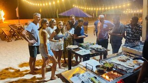 A group of people gathered around a barbecue setup with food and drinks on a sandy beach at night. - NN Beach Resort Nilaveli (Trincomalee)