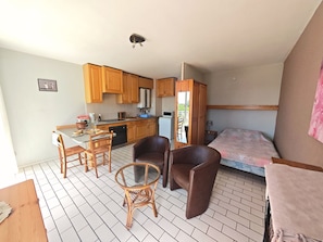 Ein kompaktes Zimmer mit Küchenzeile, einem Essbereich mit Stühlen, einem Bett und einem kleinen Tisch.