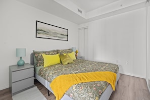 Une chambre à coucher avec un lit, une table de chevet, une lampe, un tableau encadré au mur et une porte.