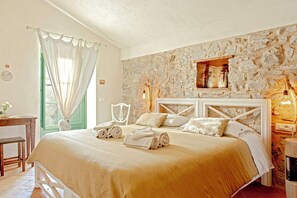 Ein Schlafzimmer mit Steinwand, einem Bett mit aufgerollten Handtüchern, einem Holz-Nachttisch und einem Fenster mit Vorhängen.