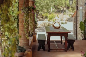 Eine Terrasse im Freien mit einem Holztisch, zwei Bänken, hängenden Pflanzgefäßen und einer Ziegelwand.