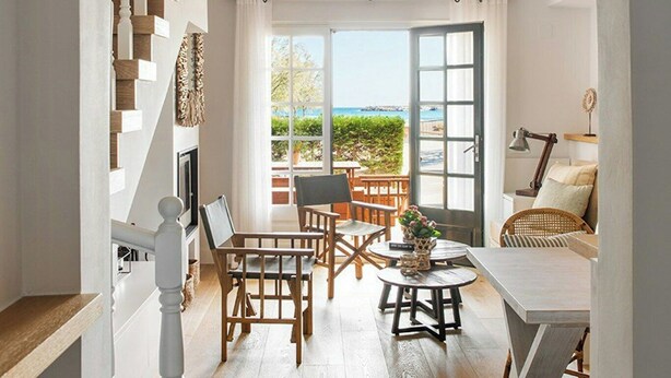 Um interior moderno com escada, sala de jantar com mobiliário de madeira e vista para o mar através de grandes janelas.