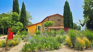 A stone building with a yellow facade, surrounded by a garden with various plants and tall trees. - Apartment in a 16th century farmhouse (Monteverdi Marittimo)