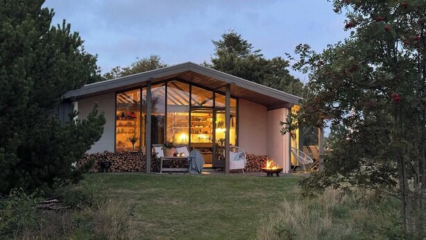 A modern house with a glass facade, a fire pit, and outdoor seating.