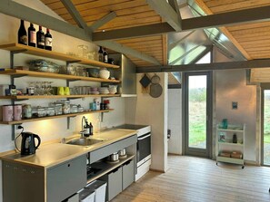 A modern kitchen with wooden beams, stainless steel appliances, and open shelving with various items. - Summer house with fields and fjord views (Thyholm)